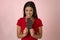 Young attractive and happy hispanic woman in red top smiling excited eating chocolate bar on pink background