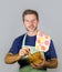 Young attractive and happy home cook man with apron and kitchen cloth grinding ingredient using mortar smiling satisfied and cheer
