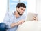 Young attractive Hispanic man at home sitting on white couch using digital tablet