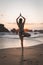 Young attractive latin woman wearing a bikini practicing hands up yoga on the beach at sunset, healthy lifestyle concept