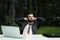 Young attractive male businessman in suit sitting at desk in forest of nature park. Stretches and rests from work.