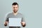 A young, attractive man holding a blank white A4 sheet, on a light background. mockup, layout, copy space