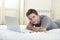 Young attractive man lying on bed or couch enjoying social networking using computer laptop at home