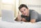 Young attractive man lying on bed or couch enjoying social networking using computer laptop at home