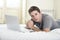 Young attractive man lying on bed or couch enjoying social networking using computer laptop at home wireless internet