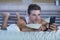 Young attractive man lying on bed happy and relaxed using internet mobile phone sending text in social media addiction