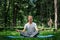 Young attractive man in sport clothes is meditating in the lotus position with a pacified face in the park