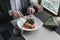 A young and attractive man uses his phone while eating veal tenderloin in ashes with grilled vegetables in an indoor