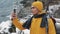 Young attractive man in yellow jacket standing in the beautiful mountains.Hiker man shooting video of winter nature. The