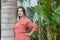 Young attractive millennial woman wearing a summer red dress while leaning against a robust palm tree