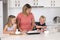 Young attractive mother preparing salad together with little son and young beautiful daughter in healthy vegetable nutrition educa