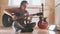 Young attractive musician plays the guitar sitting on the floor in the kitchen