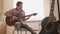 Young attractive musician plays the guitar sitting on the floor in the kitchen