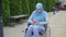 Young attractive muslim woman in a traditional scarf disabled in a wheelchair uses a smartphone sitting in the park