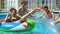 Young attractive people swimming on inflatable tubes on the pool party. Pretty women and men having a pool party. Shot