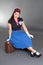 Young attractive pinup woman sitting on retro suitcase