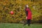 Young attractive pregnant woman in red dress, walking with small red balloon in hands and smiling. Autumn park