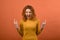 Young and attractive redhead Caucasian girl in orange jumper screaming and showing rocker gesture isolated on studio orange backgr