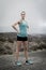 Young attractive sport woman in running singlet and shorts posing defiant and cool in asphalt road in front of mountain