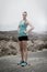 Young attractive sport woman in running singlet and shorts posing defiant and cool in asphalt road in front of mountain