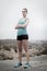 Young attractive sport woman in running singlet and shorts posing defiant and cool in asphalt road in front of mountain