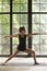 Young attractive sporty woman in Virabhadrasana II pose, window