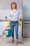 Young attractive stressed service woman in washing rubber gloves carrying cleaning bucket broom and mop frustrated and overworked