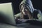 Young attractive teen woman wearing hood on hacking laptop computer cybercrime cyber crime concept