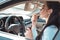 Young attractive woman applying lipstick in car, using a sun