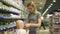 Young attractive woman with cute daughter in shopping cart choosing products in section for children at supermarket. The