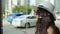 Young attractive woman in hat calls on phone at bus stop next to road.