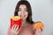 Young attractive woman holding meat burger in one hand and fried potatoes in another biting one potatoe on isolated