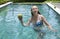 The young attractive woman with long hair in a swimwear in the pool with cocktail in coconut