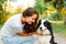 Young attractive woman playing with cute puppy dog border collie on summer outdoor background. Girl kissing holding