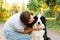 Young attractive woman playing with cute puppy dog border collie on summer outdoor background. Girl kissing holding