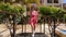 Young attractive woman in red dress with sunglasses and hat walking on the bridge over the swimming pool in the palm tree hotel ga
