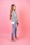 Young and attractive woman stylish model posing in jeans , high-heeled shoes and a sweater in studio on a pink