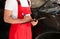 Young auto mechanic with clipboard near car in service center