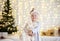 Young baby girl sitting dreaming near magical New year craft gifts by a Christmas tree