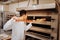 Young baker taking ready bread out of big oven in the kitchen