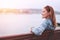 Young balanced redhead woman sitting on bench at riverside looking away in sunset