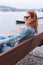 Young balanced redhead woman sitting on bench at riverside side view