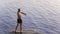 Young bald caucasian man standing in river and throwing rocks in the water