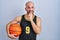 Young bald man with beard wearing basketball uniform holding ball thinking worried about a question, concerned and nervous with