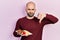 Young bald man eating fresh and healthy fruits with angry face, negative sign showing dislike with thumbs down, rejection concept