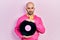 Young bald man holding vinyl disc relaxed with serious expression on face