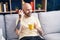 Young bald man listening voice message by smartphone drinking coffee at home