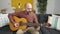 Young bald man playing classical guitar sitting on sofa at home
