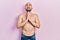 Young bald man standing shirtless begging and praying with hands together with hope expression on face very emotional and worried