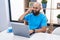 Young bald man using laptop talking on smartphone at home